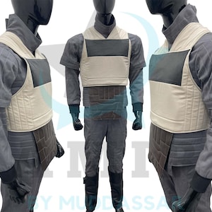 Puede incluir: Un chaleco gris y blanco con un diseño acolchado. El chaleco tiene un panel marrón en la parte delantera y un panel negro en la parte posterior. El chaleco se lleva sobre una camisa gris.
