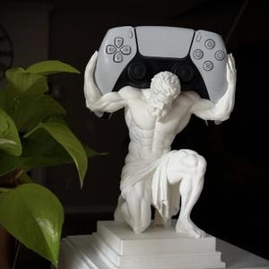 Pode incluir: Uma estátua branca de uma figura ajoelhada com constituição musculosa, segurando um comando de videojogo branco e preto acima da cabeça. A figura está posicionada sobre uma base quadrada branca, exibindo detalhes anatómicos precisos.