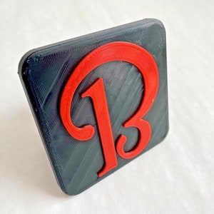 May include: A black square-shaped object with a red 3D letter "B" in the center.