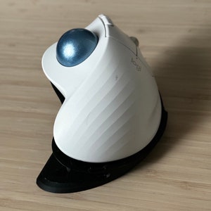 May include: A white ergonomic trackball mouse with a blue trackball and a black base. The mouse has a Logitech logo on the side.