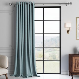 May include: A light blue curtain with a textured weave hangs from a silver curtain rod in front of a window with a view of a green field and trees.