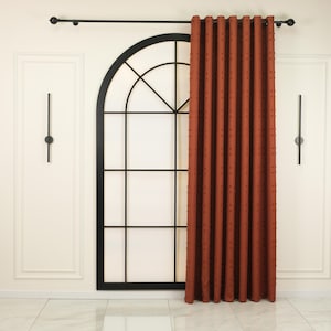 May include: Rust-colored curtain with a textured dot pattern, hanging from a black rod. The curtain is next to a black arched window frame. The room has white walls and a marble floor.