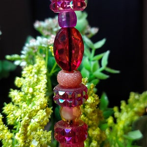 May include: A pink and red beaded tower with a crystal-like top. The beads are various shapes and sizes, including round, oval, and faceted.