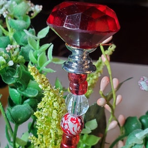 May include: A red glass bead with a silver metal top and a red diamond-shaped glass bead. The beads are strung on a wire with other red and white glass beads.