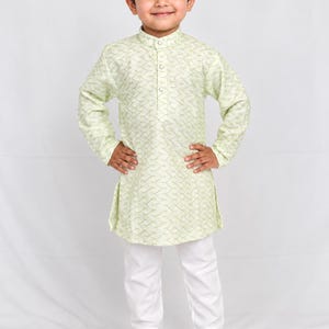 May include: A light green long-sleeved kurta featuring a subtle repeating chevron pattern, a mandarin collar, and a partial button-down front, paired with plain white trousers and brown leather closed-toe sandals.