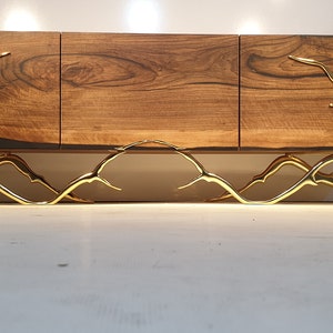 May include: A wooden cabinet with three doors and gold metal legs. The cabinet has a dark wood finish and the legs are shaped like branches.