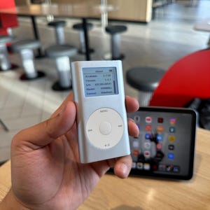 Może przedstawiać: Srebrny odtwarzacz multimedialny iPod z białym pokrętłem sterowania i małym ekranem wyświetlającym informacje o urządzeniu. Ekran pokazuje 3,7 GB dostępnej pamięci. Czarny tablet znajduje się w tle.