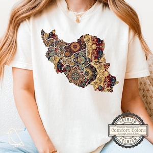 May include: Cream-colored t-shirt featuring a detailed map of Iran, filled with a colorful, patterned design in shades of red, gold, and blue. The shirt has a vintage look and feel, with a Comfort Colors label.