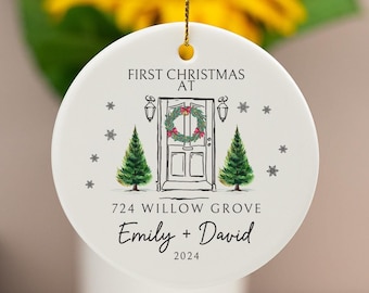 Könnte beinhalten: Weißer Keramik-Weihnachtsbaumschmuck mit einer handgezeichneten Illustration einer Haustür mit einem Kranz, zwei Tannenbäumen und Schneeflocken. Der Text lautet "First Christmas at 724 Willow Grove Emily + David 2024".