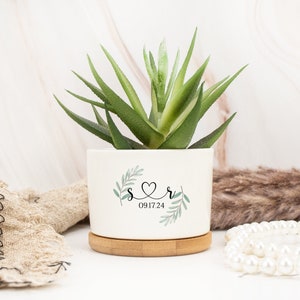 May include: White ceramic planter with a bamboo base. The planter has a green leafy design with the letters "S" and "R" connected by a heart and the date "09.17.24" printed on it.