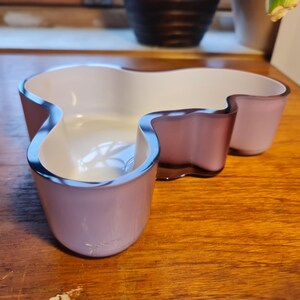 May include: A white and purple glass bowl with an abstract, organic shape. The bowl is made of two pieces of glass, one white and one purple, that are joined together.