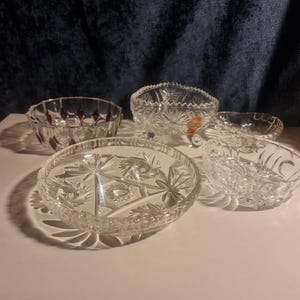 Könnte beinhalten: Vier klare Glasschalen mit aufwendigen Schnitzereien. Die Schalen sind auf einer hellbraunen Oberfläche angeordnet.