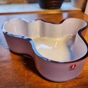 May include: A white and purple glass bowl with a wavy, organic shape. The bowl has a black rim and the iittala logo on the bottom.
