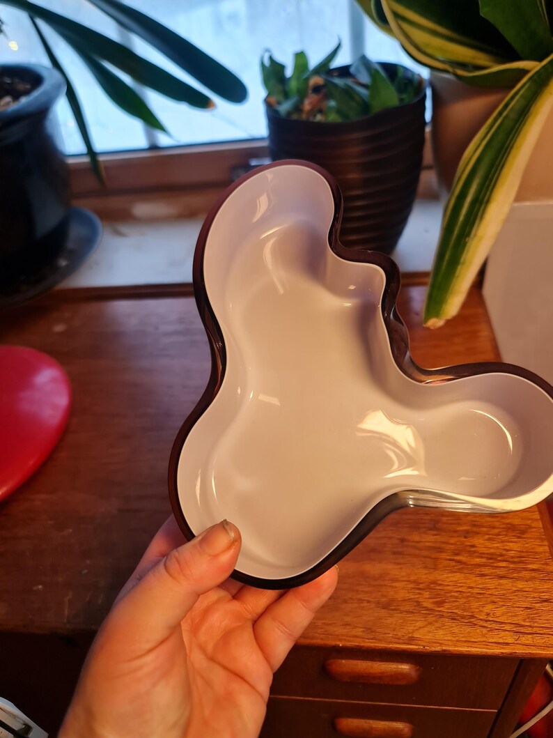 May include: A purple glass bowl with a dark brown rim. The bowl has an organic, free-form shape.