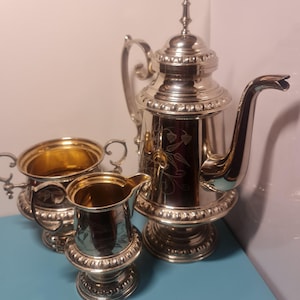 Puede incluir: Un juego de té de plata con tetera, jarra de crema y azucarero. El juego tiene un diseño floral y está en excelentes condiciones.