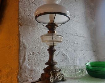 May include: A vintage brass oil lamp with a white glass shade. The lamp has a decorative base with intricate details and a clear glass oil reservoir.