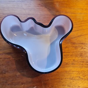 May include: A purple glass bowl with a unique, organic shape. The bowl has a smooth, white interior and a dark purple rim.