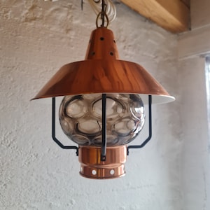 May include: A copper pendant light with a round, textured glass shade. The light is hanging from a chain and has a black metal frame.