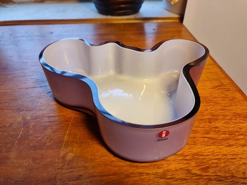 May include: A purple and white glass bowl with a wavy edge and the iittala logo.