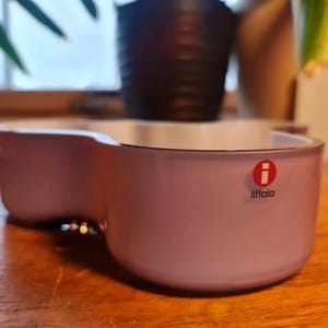 May include: A light purple glass bowl with a rounded, organic shape. The bowl has a white interior and features the Iittala logo on the front.