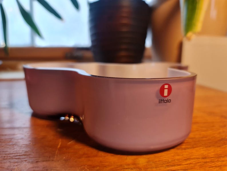 May include: A light purple glass bowl with a rounded, organic shape. The bowl has a white interior and features the Iittala logo on the front.