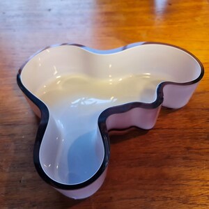 May include: A white and purple glass bowl with a unique, organic shape. The bowl has a black rim and is perfect for serving snacks or holding decorative items.