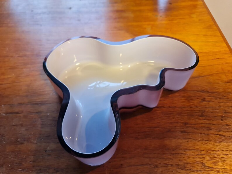 May include: A white and purple glass bowl with a unique, organic shape. The bowl has a black rim and is perfect for serving snacks or holding decorative items.