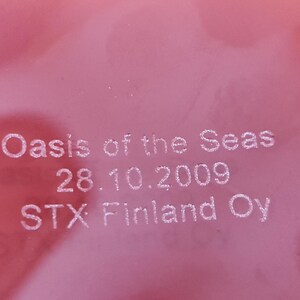 May include: Close-up of a red surface with white text that reads "Oasis of the Seas 28.10.2009 STX Finland Oy".