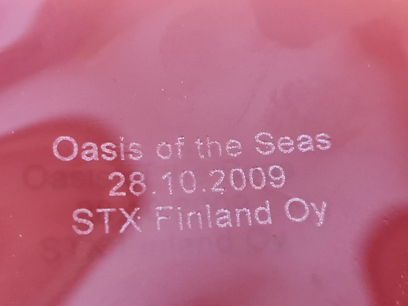 May include: Close-up of a red surface with white text that reads "Oasis of the Seas 28.10.2009 STX Finland Oy".