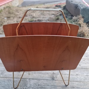 Puede incluir: Un revistero vintage de teca con un marco de latón y un asa de cuerda blanca. El revistero tiene dos estantes y está en buen estado.