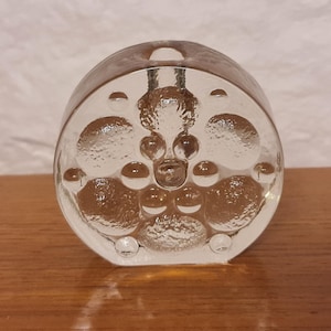Pode incluir: Um vaso de vidro transparente com um design redondo e texturizado. O vaso tem uma série de pequenas bolhas redondas que criam um padrão único.