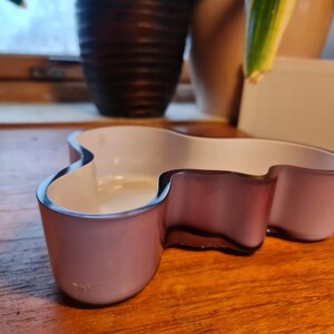 May include: A light purple glass bowl with an irregular, organic shape. The bowl has a white interior and a smooth, glossy finish.