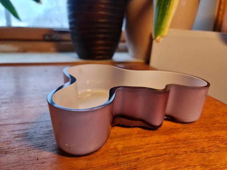 May include: A light purple glass bowl with an irregular, organic shape. The bowl has a white interior and a smooth, glossy finish.