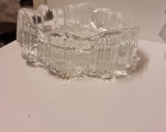 May include: A clear glass ashtray with a textured, rippled design. The ashtray is round and has a slightly raised edge.