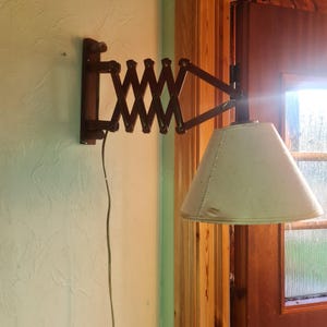 Könnte beinhalten: Eine braune, an der Wand montierte Lampe aus Holz mit einem weißen Stoffschirm. Die Lampe hat einen klappbaren Arm, der verstellt werden kann, um das Licht zu lenken.