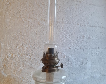 May include: A vintage glass oil lamp with a brass burner and a clear glass chimney. The lamp has a simple design and is in good condition.