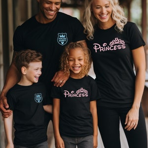 May include: A family of four wearing black t-shirts with a Disney theme. The adults' shirts say "Princess" and "Princess Security Detail" in pink and blue lettering. The children's shirts say "Princess" in pink lettering.