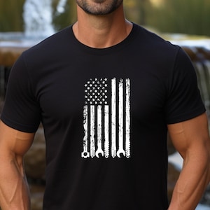 May include: Black t-shirt with a white distressed American flag design featuring tools as the stripes.