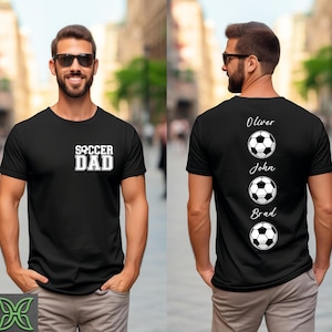 Peut inclure: T-shirt noir avec l'inscription "SOCCER DAD" en lettres blanches. Le dos du t-shirt pr&eacute;sente trois ballons de football avec les noms Oliver, John et Brad au-dessus de chaque ballon. Le t-shirt est &agrave; col rond.
