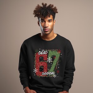 Może przedstawiać: Czarna bluza z napisem "six" i "seven" w czerwonym i zielonym brokatem, obramowanym światełkami i płatkami śniegu. Bluza z okrągłym dekoltem.