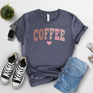 May include: A navy blue t-shirt with the word "COFFEE" printed in pink, brown, and orange letters with a small pink heart below the word.