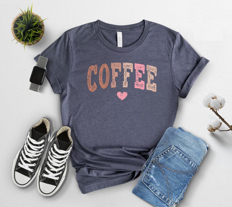 May include: A navy blue t-shirt with the word "COFFEE" printed in pink, brown, and orange letters with a small pink heart below the word.
