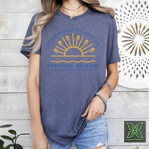 May include: A blue t-shirt with a yellow sun and arrows graphic. The text reads "Celebrate, Educate, Advocate. Everyone Belongs. World Down Syndrome Day 2021."