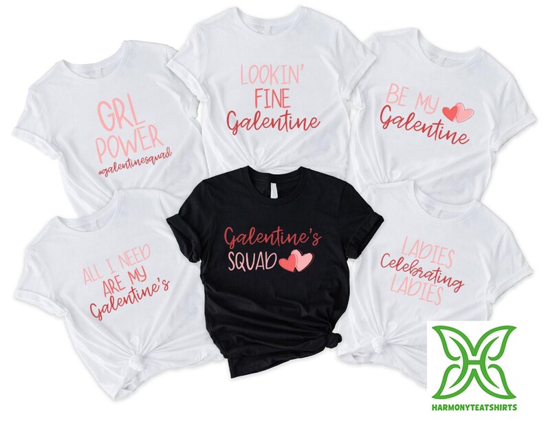 May include: White and black t-shirts with pink text and graphics. The shirts have phrases like "GRL POWER," "LOOKIN' FINE Galentine," and "Galentine's SQUAD." The shirts are for a Galentine's Day theme.