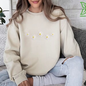 a woman sitting on a couch wearing a sweater with daisies on it