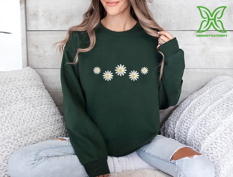 a woman sitting on a bed wearing a green sweater with daisies on it