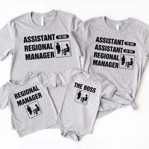 K&ouml;nnte beinhalten: Ein Familienset aus hellgrauen T-Shirts und einem Body. Die Shirts tragen schwarzen Text: "Assistent des Regionalleiters", "Regionalleiter" und "Der Boss". Jedes Kleidungsst&uuml;ck hat eine kleine Grafik.