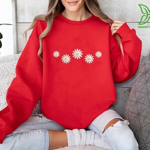 a woman sitting on a couch wearing a red sweatshirt with daisies on it