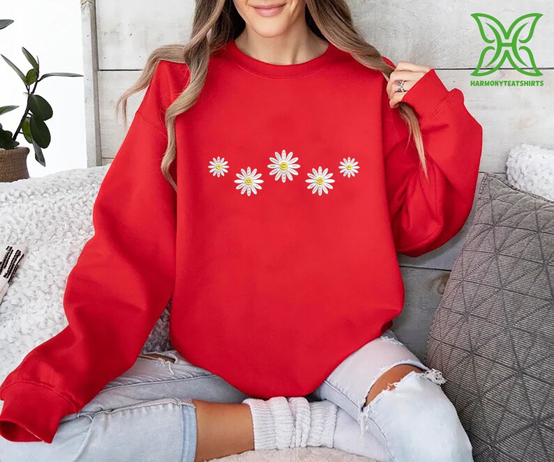 a woman sitting on a couch wearing a red sweatshirt with daisies on it