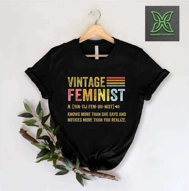 May include: Black t-shirt with a vintage-style graphic that reads "Vintage Feminist" with a definition and pronunciation. The graphic is in rainbow colors.